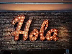 Illuminated "Hola" sign on brick wall.